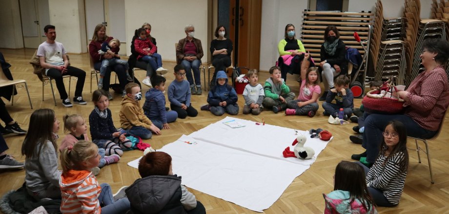 Kinder im Kreis auf dem Boden sitzend, Weißes Laken in der Mitte mit einem Storch