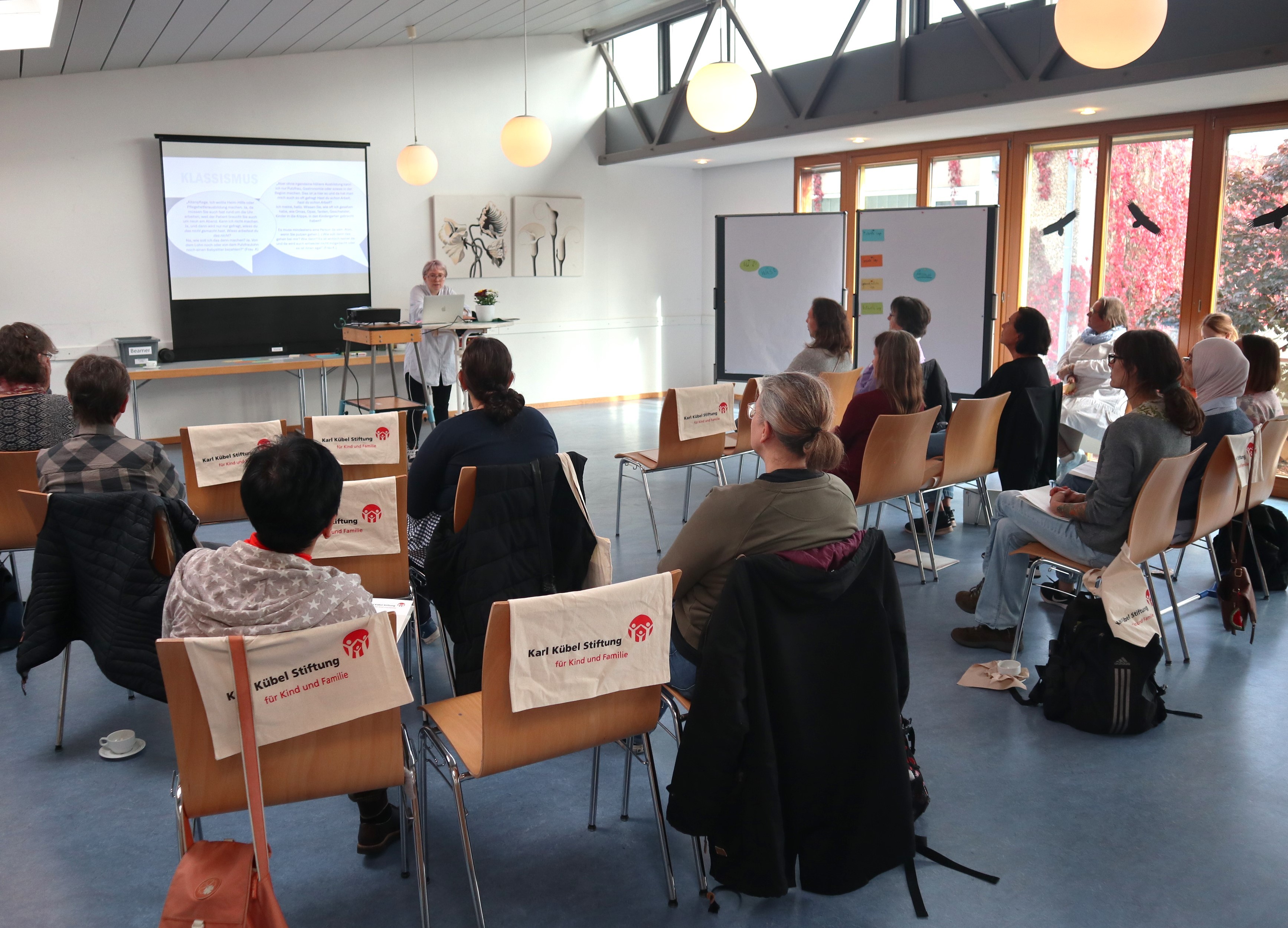 Erwachsene sitzen in einem Raum und schauen auf eine Leinwand.