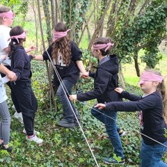 Kinder mit verbundenen Augen hangeln sich im Wald an einem Seil entlang