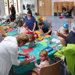 Viele Mütter basteln mit ihren kleinen Kindern Geschenke an einem großen Tisch