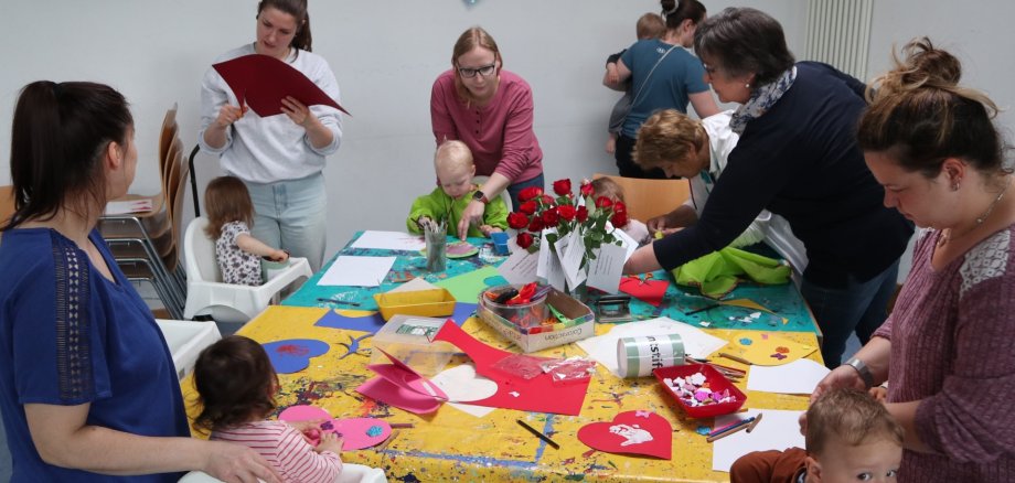 Viele Mütter basteln mit ihren kleinen Kindern Geschenke an einem großen Tisch