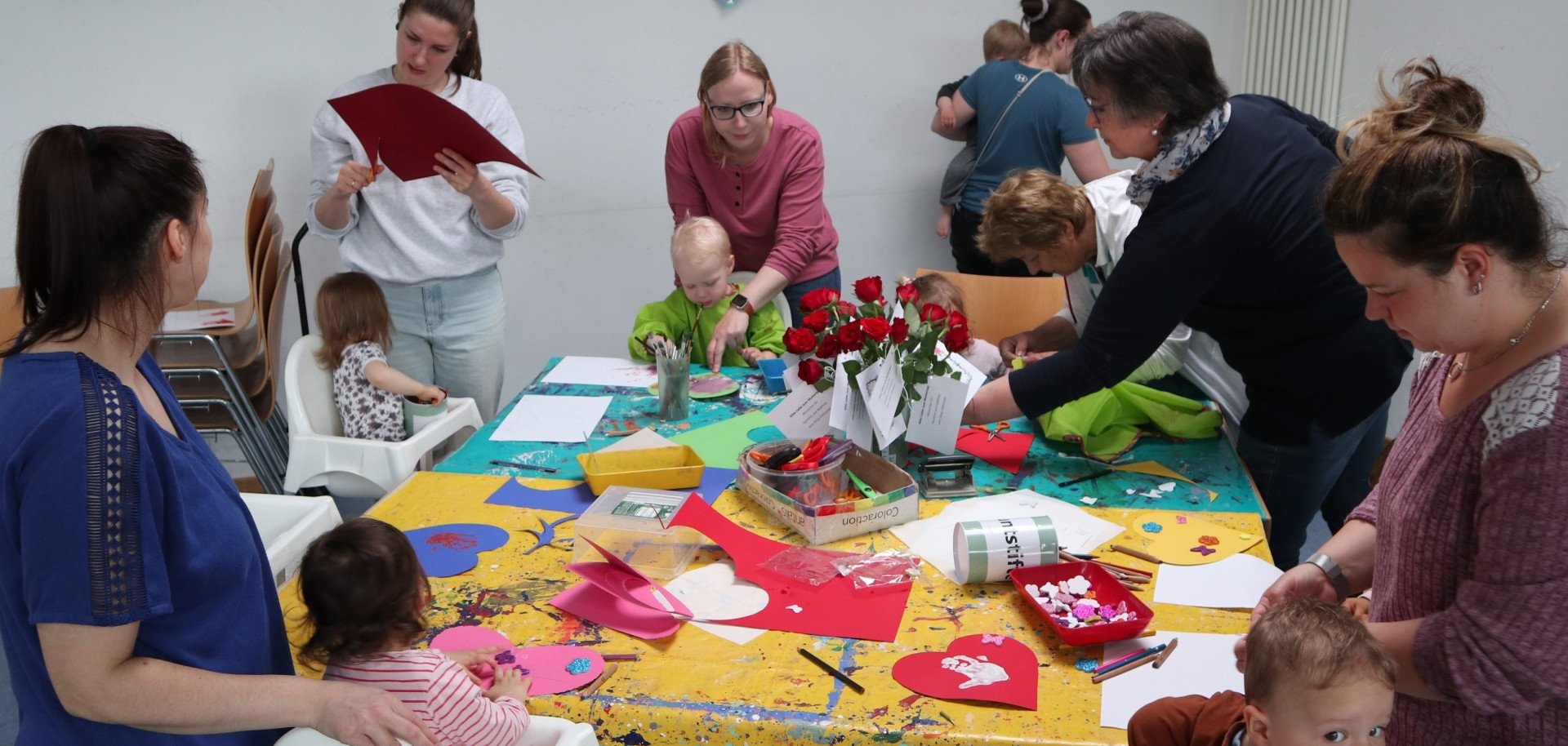 Viele Mütter basteln mit ihren kleinen Kindern Geschenke an einem großen Tisch