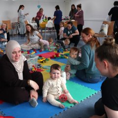 Mütter sitzen mit ihren kleinen Kindern auf dem Boden und spielen 