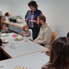 Mütter mit ihren Kindern und ein Mann sitzen am Tisch und essen Kuchen