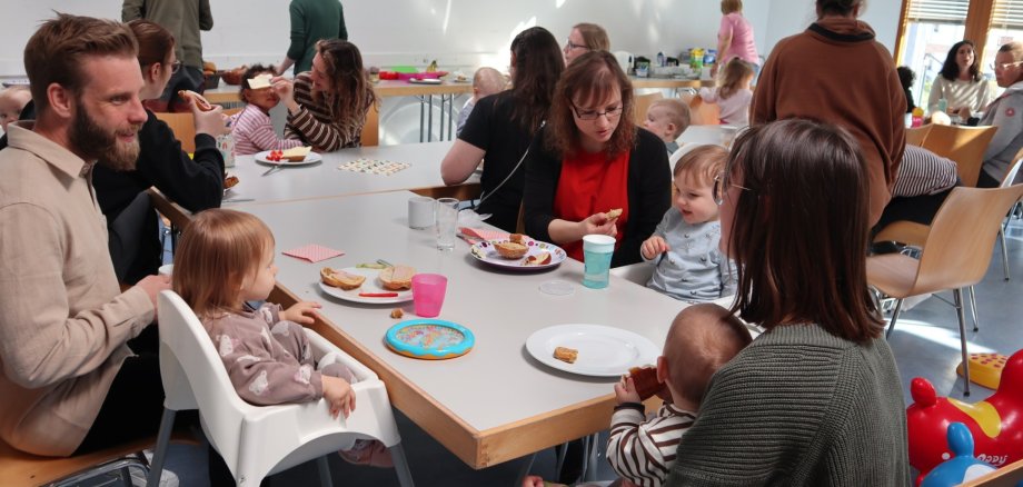 Mütter mit ihren Kindern und ein Mann sitzen am Tisch und essen Kuchen