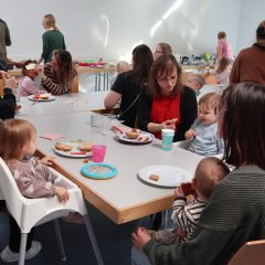 Mütter mit ihren Kindern und ein Mann sitzen am Tisch und essen Kuchen
