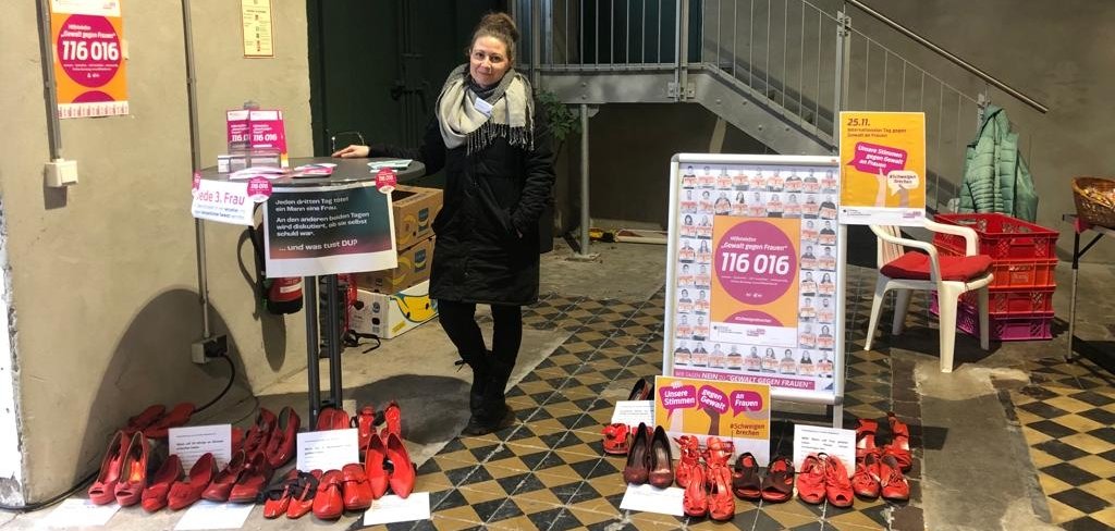 Infostand auf dem Wochenmarkt Eine Frau steht an einem Tisch. Im Vordergrund viele rote Schuhpaare.