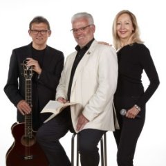 Ein Mann mit Gitarre, eine Frau mit Mikrofon und ein Mann mit einem Buch in der Hand