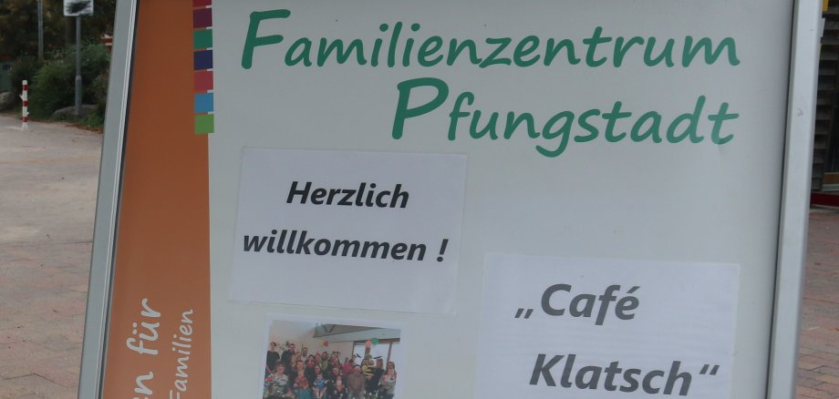 Hinter einem Werbeschild steht eine Frau mit einem Bollerwagen