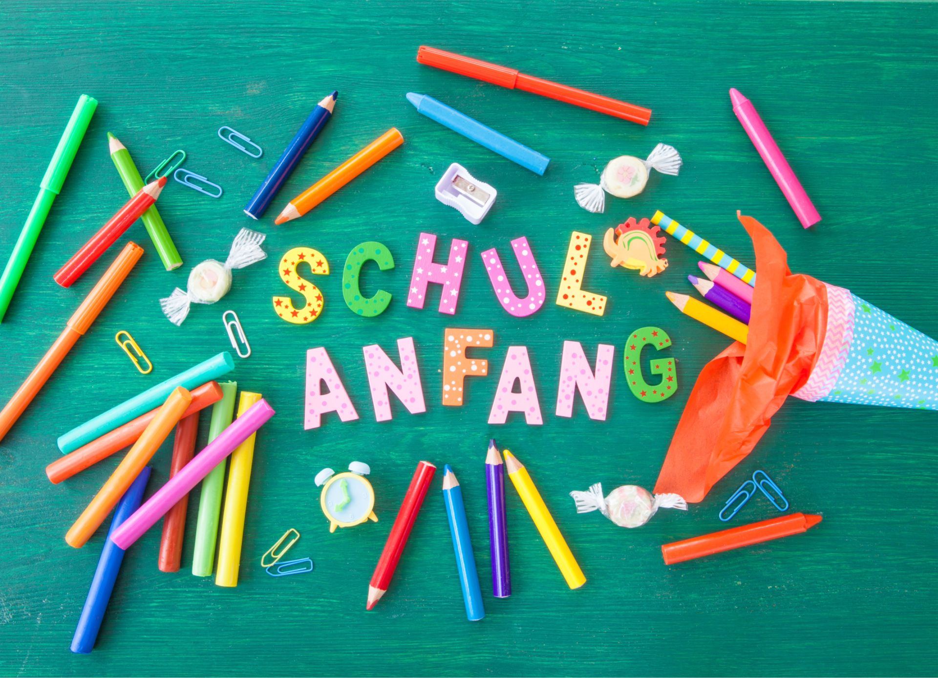 Schulanfang, Schultüte mit bunten Stiften auf grünem Hintergrund