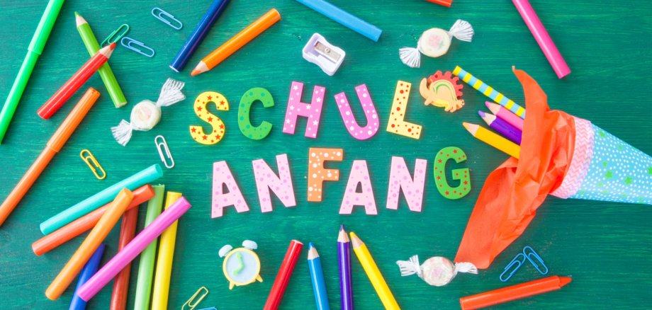 Schulanfang, Schultüte mit bunten Stiften auf grünem Hintergrund