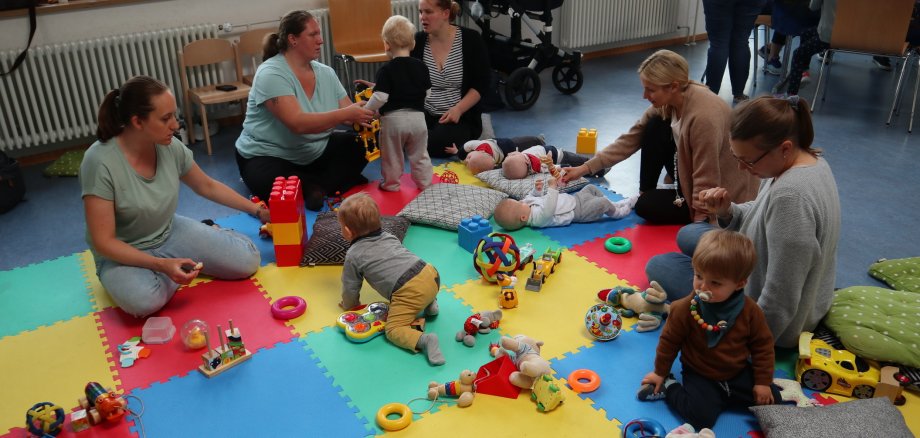 Kinder und Mütter im Kreis auf dem Boden sitzend, Spielzeug
