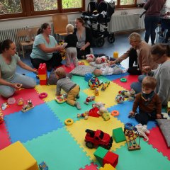 Spielende Kinder mit ihren Mamas auf bunten Matten auf dem Boden, Spielzeug