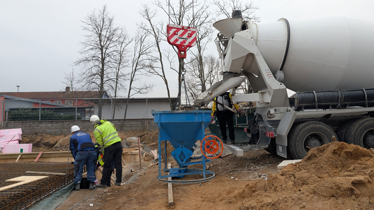 Zwei Bauarbeiter und ein Betonbischer, der Beton in einen Trichter füllt