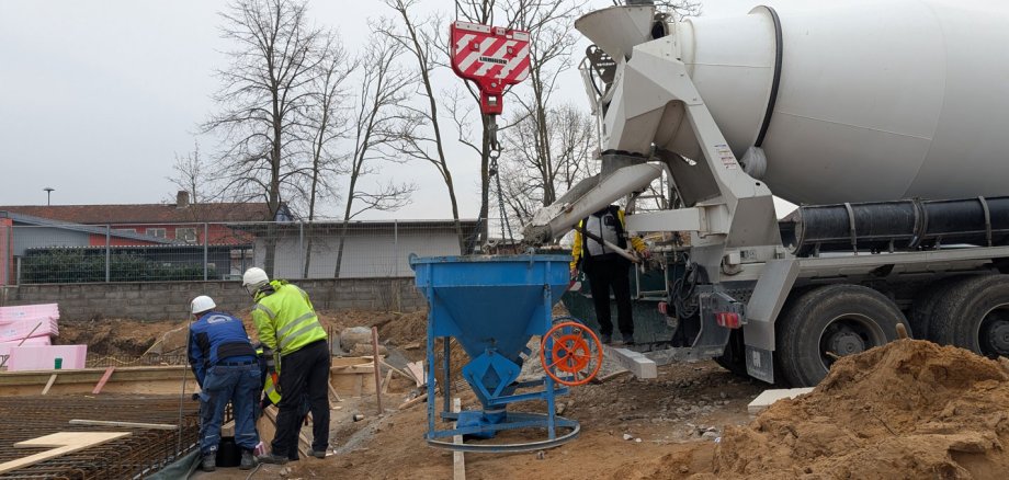 Zwei Bauarbeiter und ein Betonbischer, der Beton in einen Trichter füllt
