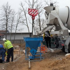 Zwei Bauarbeiter und ein Betonbischer, der Beton in einen Trichter füllt