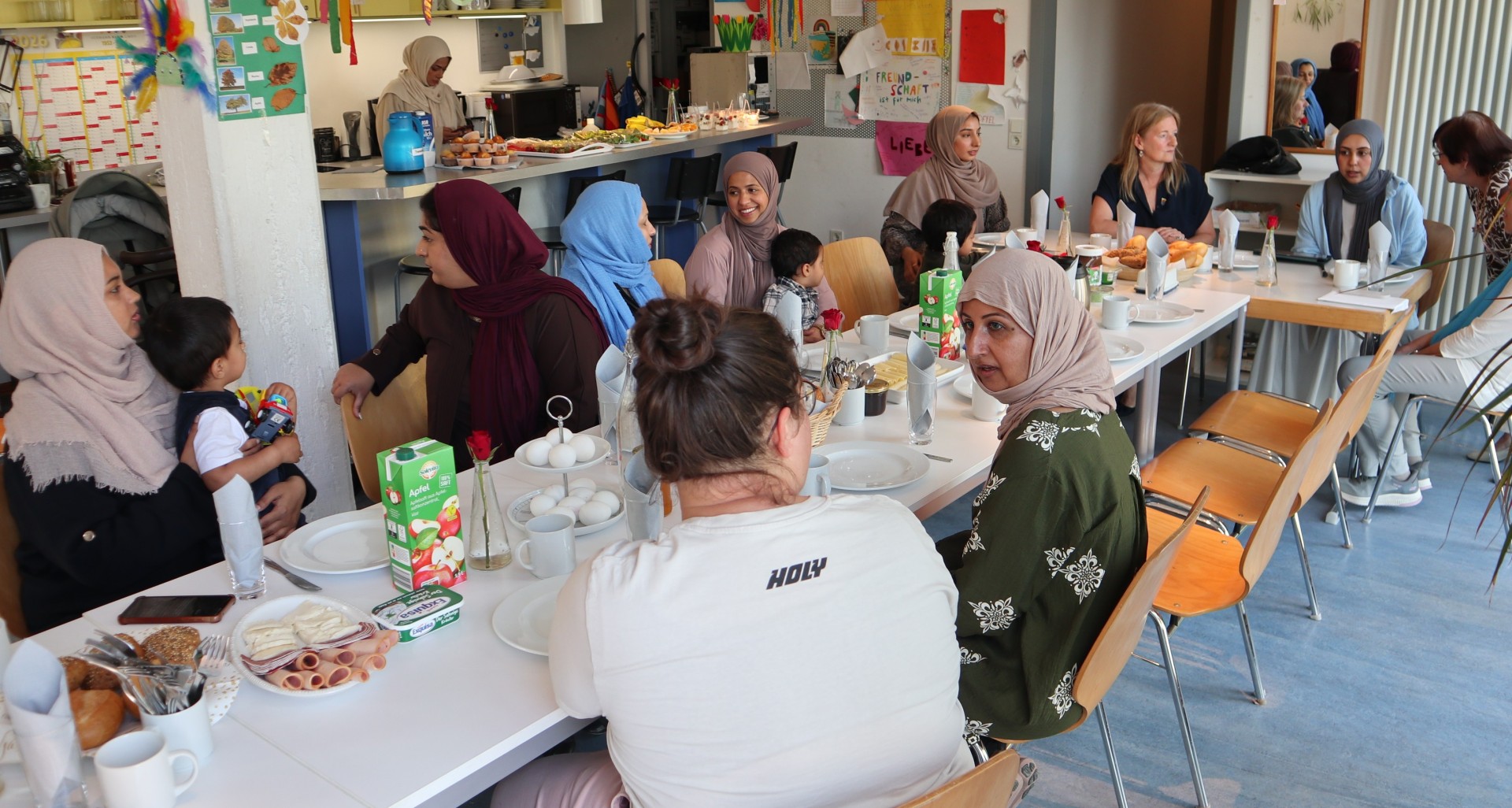 Neues Frauen-Café im Familienzentrum Pfungstadt Viele Frauen sitzen mit ihren Kindern bei Kaffee und Kuchen an einem langen Tisch und unterhalten sich.