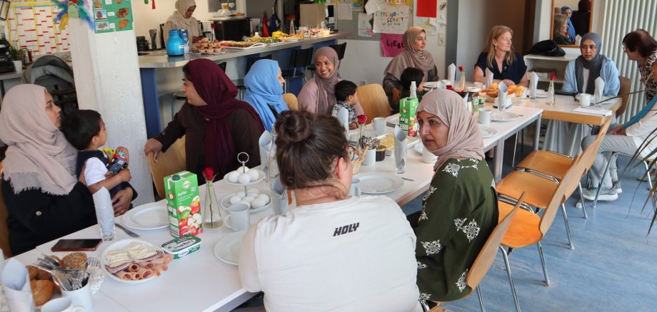 Neues Frauen-Café im Familienzentrum Pfungstadt Viele Frauen sitzen mit ihren Kindern bei Kaffee und Kuchen an einem langen Tisch und unterhalten sich.