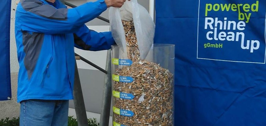 Ein Mann wirft einen Sack voller Zigarettenkippen in einen durchsichtigen Behälter