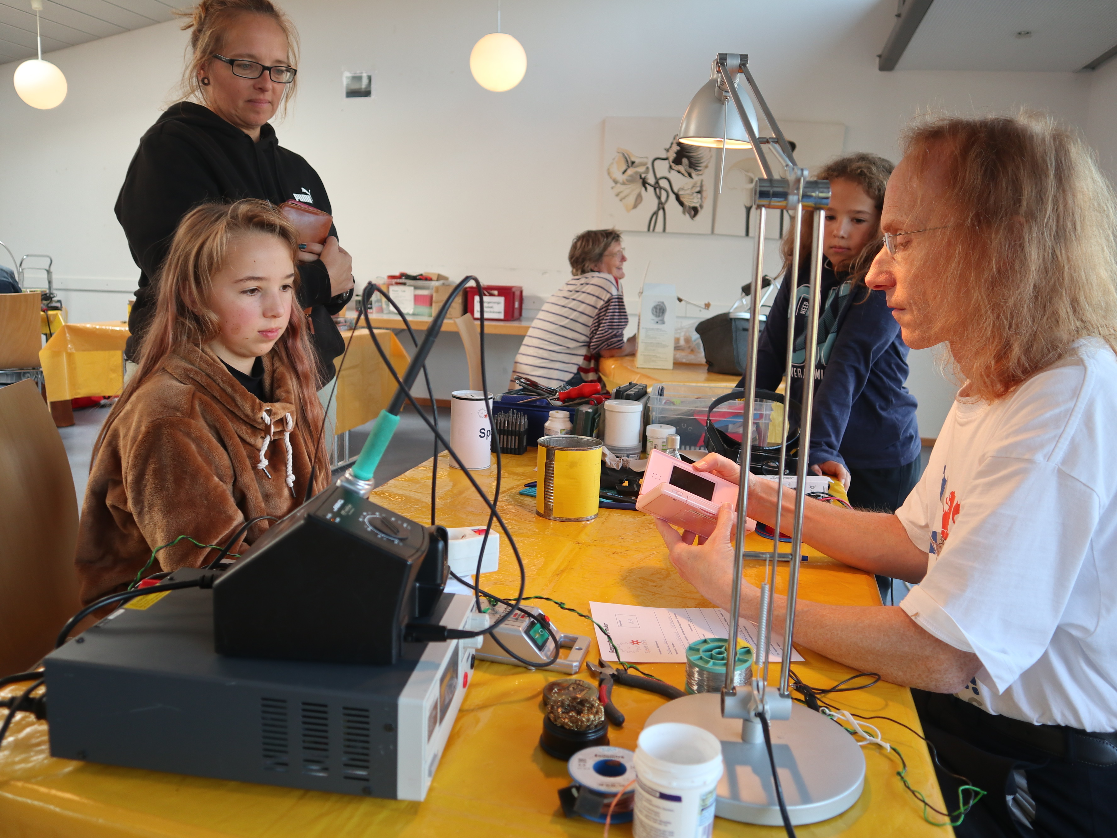Zwei Kinder und ihre Mutter lassen von einem Mann einen rosa Gameboy reparieren