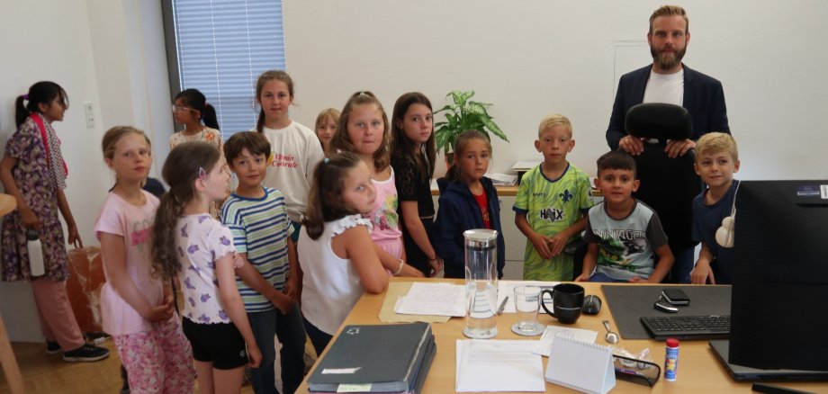 Gruppenfoto Bürgermeister und Kinder im Büro des Bürgermeisters hinter einem Schreibtisch. 