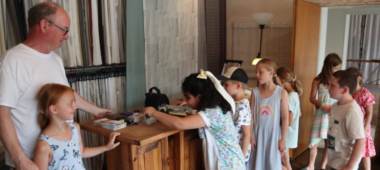 Mehrere Kinder begutachten etwas, das sich auf einem Tisch beim Raumausstatter-Meister Frank Neeb befindet. Dieser steht mit seiner Tochter Naila daneben und beobachtet das Geschehen.