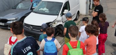 Kinder begutachten einen Unfallschaden an einem Auto.