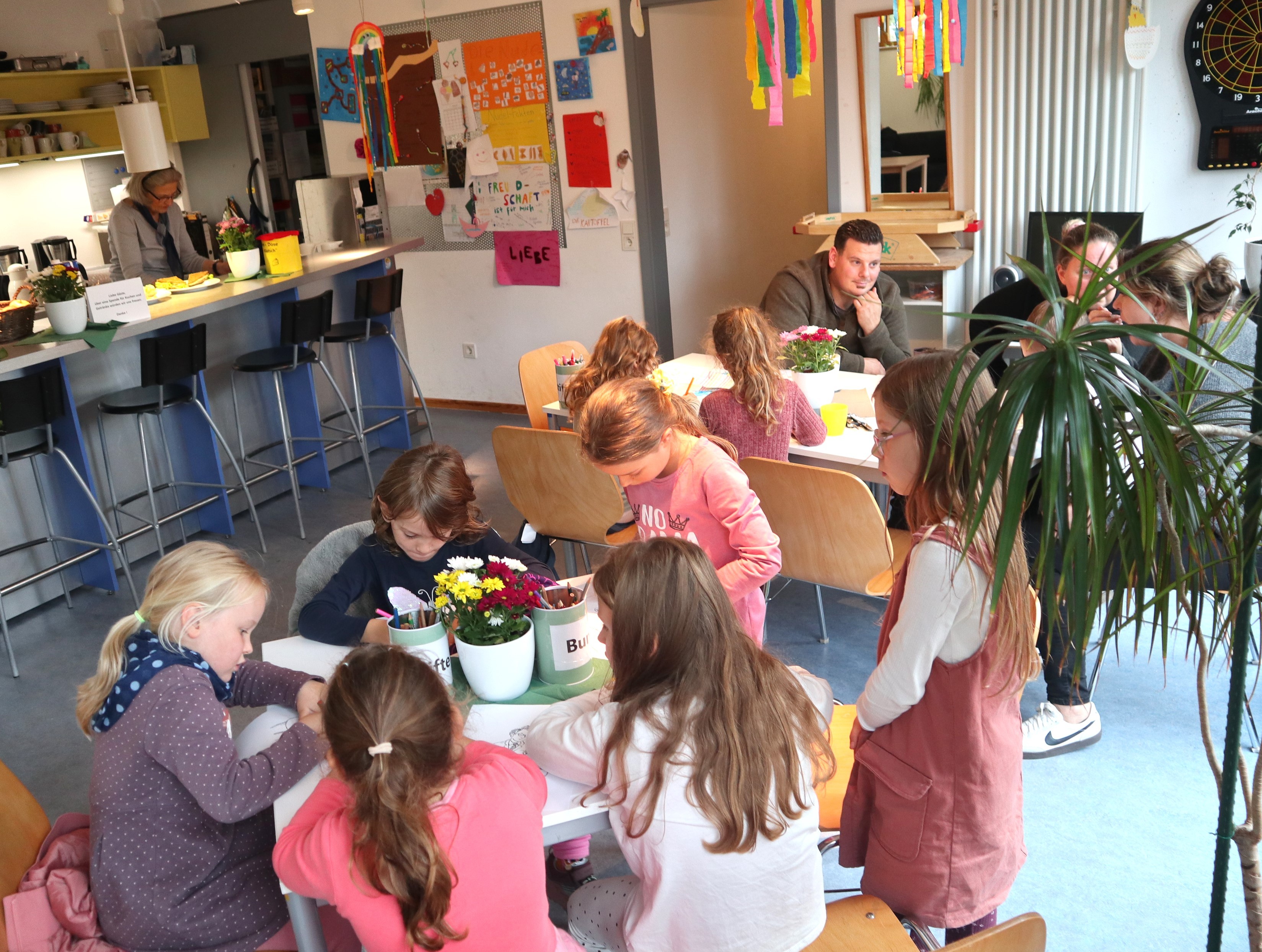 Kinder und Eltern sitzen an Tischen, malen und essen Kuchen