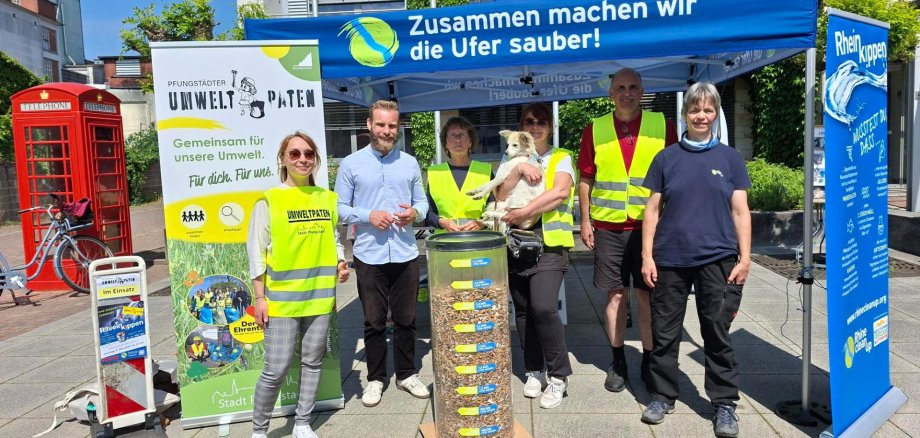 Gruppenbild mit Männern und Frauen sowie einem Hund, davor ein großer Behälter mit gesammelten Zigarettenkippen