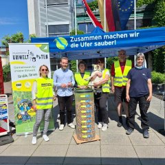 Gruppenbild mit Männern und Frauen sowie einem Hund, davor ein großer Behälter mit gesammelten Zigarettenkippen