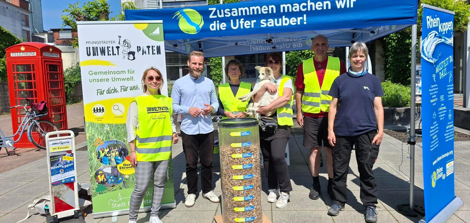 Gruppenbild mit Männern und Frauen sowie einem Hund, davor ein großer Behälter mit gesammelten Zigarettenkippen
