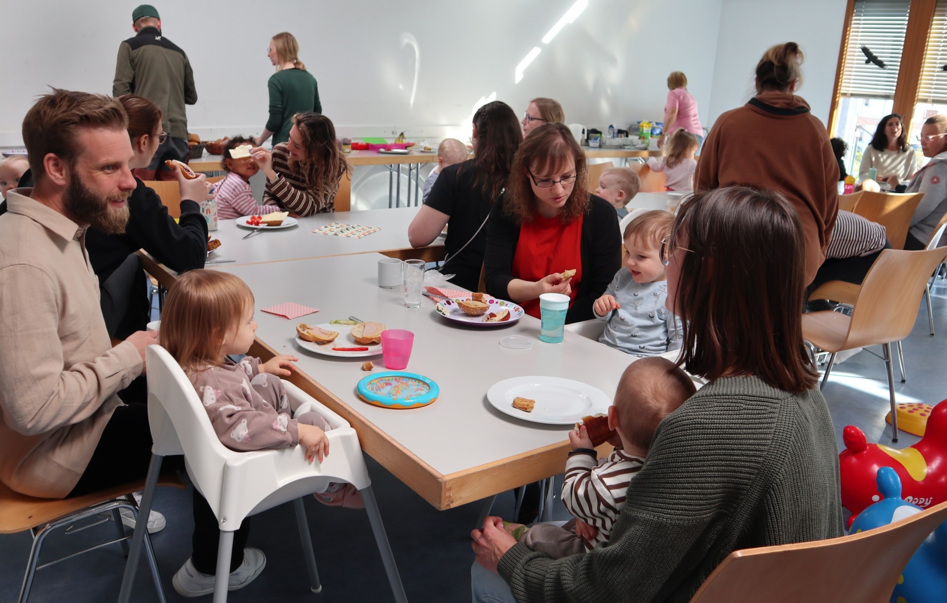Mütter mit ihren Kindern und ein Mann sitzen am Tisch und essen Kuchen