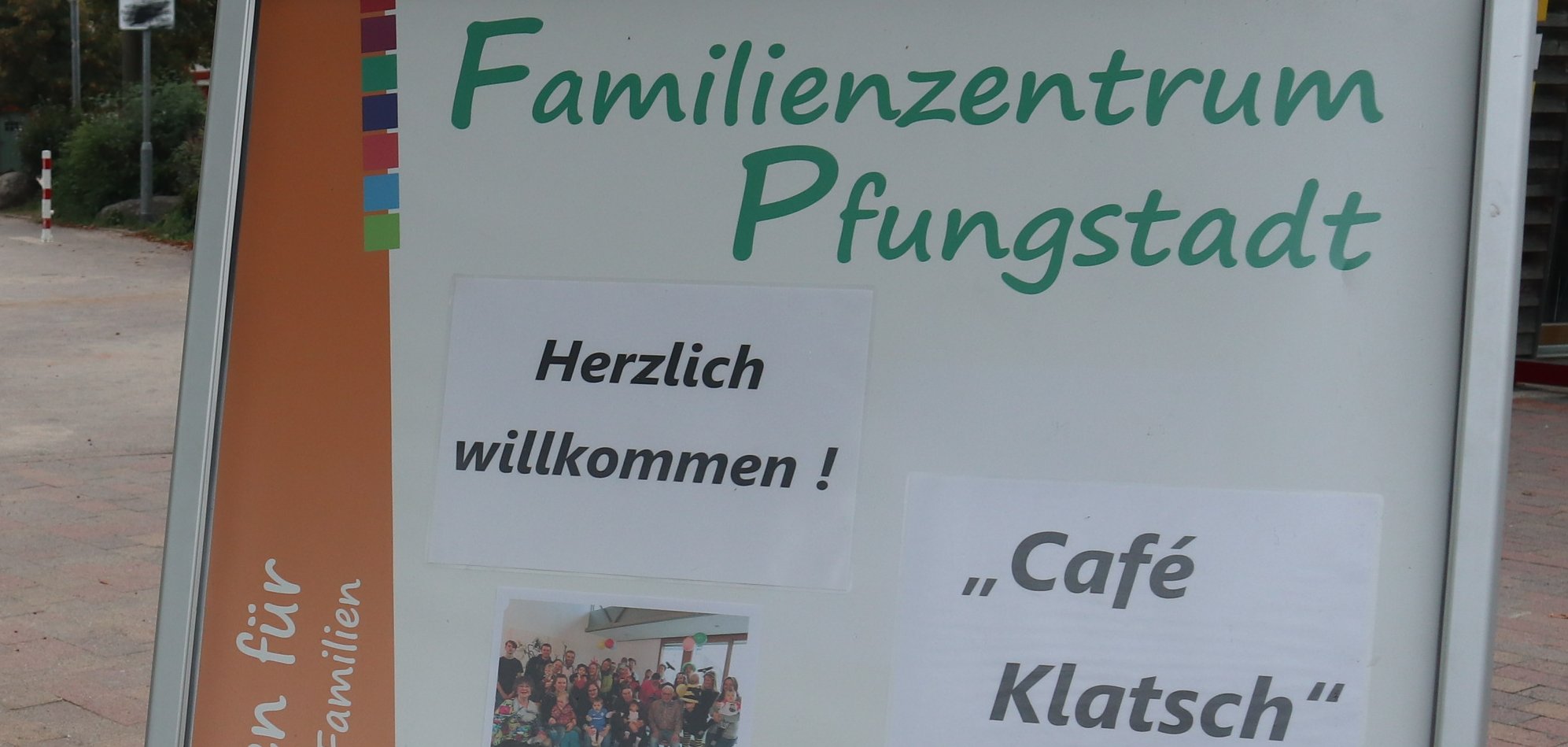Hinter einem Werbeschild steht eine Frau mit einem Bollerwagen
