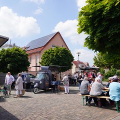 Pfungstädter Naschmarkt Menschen sitzen an Tischen inmitten des Marktes und genießen Getränke und Essen